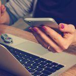 Photo of woman looking at her iphone in front of a laptop by William Iven on Unsplash